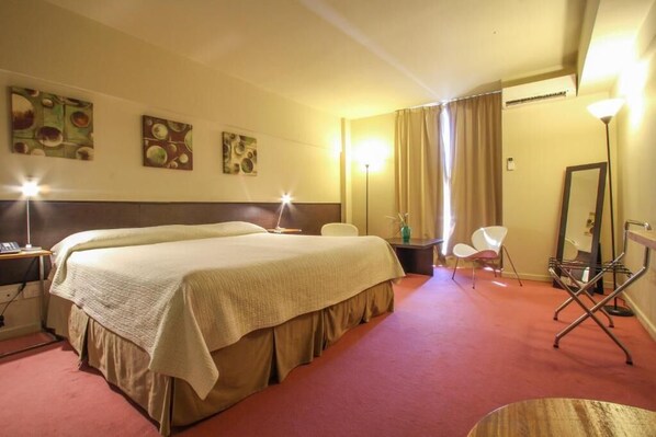 Una habitación de hotel con una cama grande, mesitas de noche, una silla, un escritorio y un espejo.