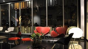 Un comedor moderno con sillas rojas y blancas, una mesa oscura y un ventanal con reflejos.