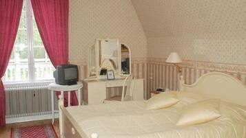 Un dormitorio con cama, escritorio, televisor y ventana con cortinas.