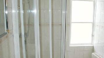A bathroom with a glass-enclosed shower, a sink, and a window.