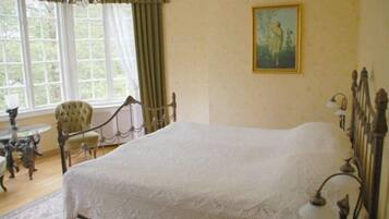 A room with a large bed, a chair, a table, and a painting on the wall.