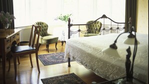 A bedroom with a large bed, two chairs, a dresser, and a chandelier. - Solvikens Pensionat (Ingelstad)