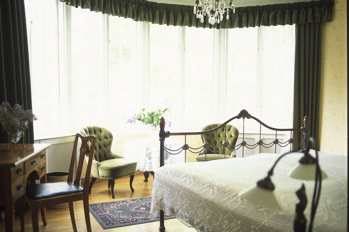 Un dormitorio con una cama grande, dos sillones, un aparador y una araña.