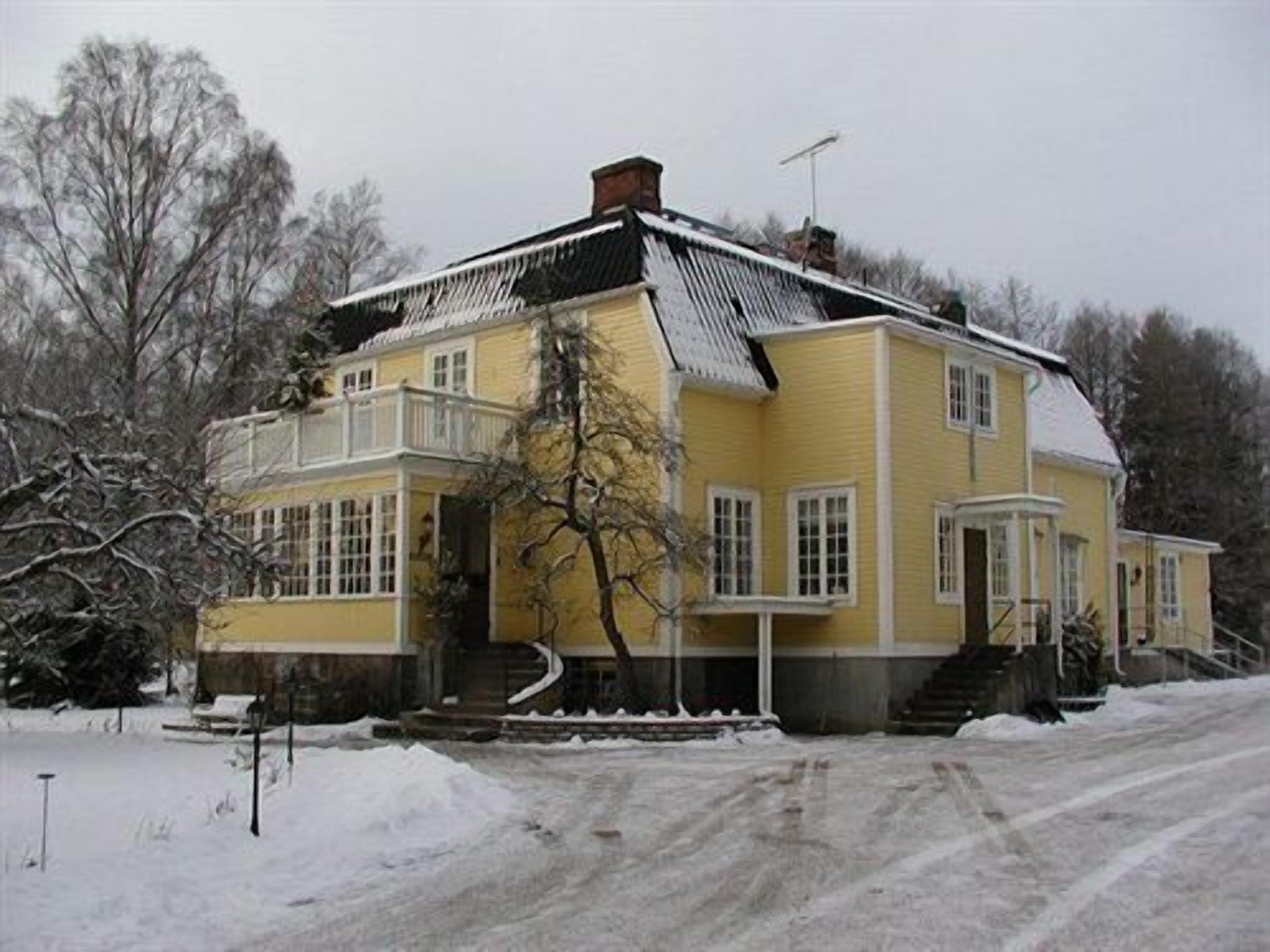Una casa amarilla con balcón, chimenea y tejado cubierto de nieve.