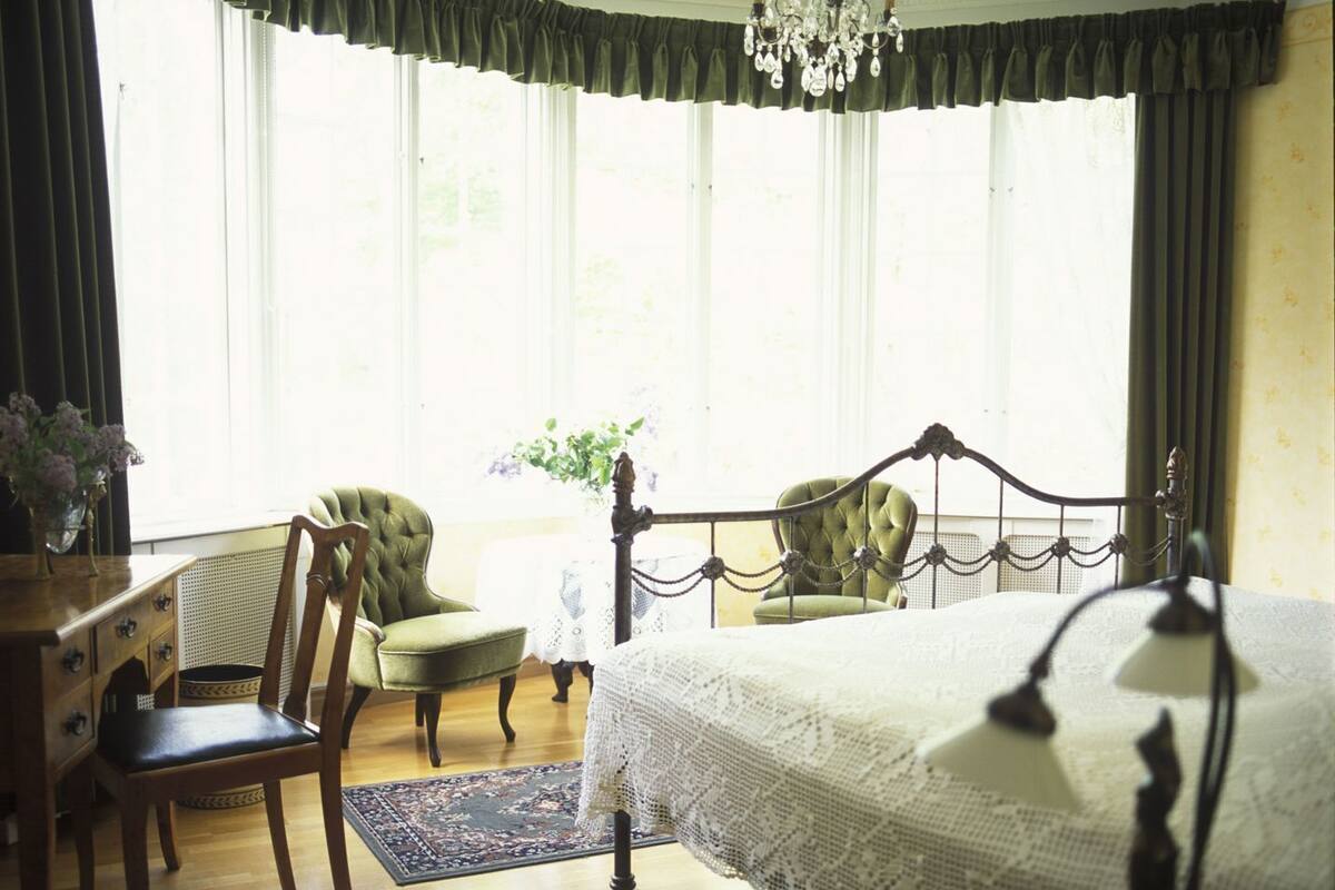 Un dormitorio con una cama grande, una araña de cristal, dos sillas, un tocador y una ventana con cortinas.