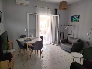 A modern living room with a sofa, a dining table with chairs, a TV, and a painting on the wall. - Asprokavos Beach Apartment (Corfu)