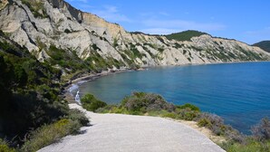 A coastal road with a paved path leading to a beach, surrounded by cliffs and greenery. - Asprokavos Beach Apartment (Corfu)