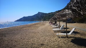 A beach with lounge chairs and a thatched-roof structure. - Asprokavos Beach Apartment (Corfu)