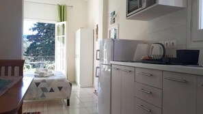 Una habitación pequeña y luminosa con cama, mesa de comedor y kitchenette.