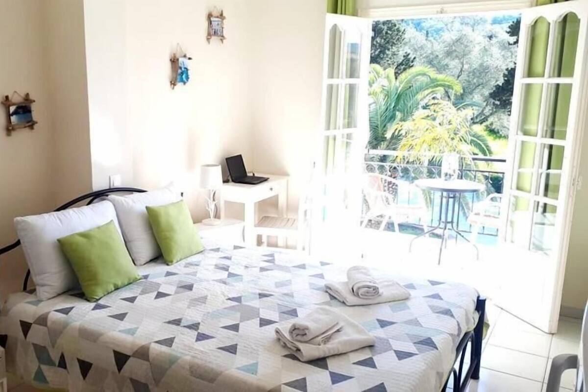Un dormitorio con cama, un escritorio y vistas a un balcón con mobiliario exterior.