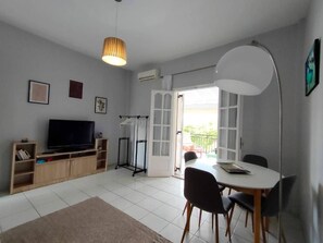 Una sala moderna con televisor de pantalla plana, mueble de entretenimiento de madera, mesa de comedor con sillas y un gran ventanal con vistas.