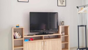 A television on a wooden stand with shelves, a framed picture on the wall, and a coat rack. - Asprokavos Beach Apartment (Corfu)
