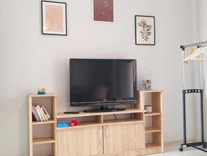 A television on a wooden stand with shelves, a framed picture on the wall, and a coat rack. - Asprokavos Beach Apartment (Corfu)
