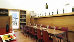Un restaurante con una larga mesa de madera, sillas rojas y una estantería para vinos en la pared.
