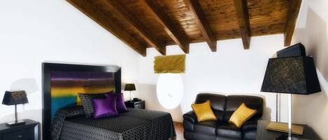A bedroom with a bed, a black leather sofa, a nightstand, a lamp, and a window with a view.