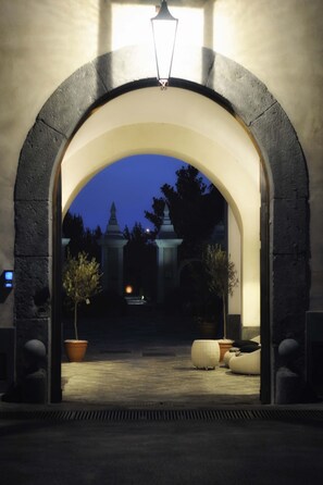 An arched entrance to a building at twilight with a lamp above it, potted plants, and a bench. - Relais Villa Buonanno (Cercola)