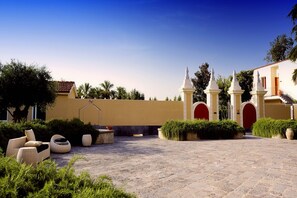 A courtyard with a yellow building, a white structure with pointed tops, and outdoor seating. - Relais Villa Buonanno (Cercola)