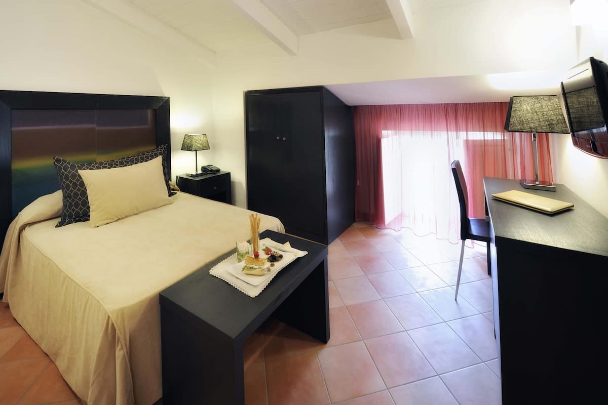 A hotel room with a bed, a desk, a chair, a wardrobe, and a window with curtains.