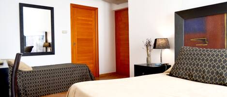 A hotel room with a bed, two bedside tables, a chair, a desk, a mirror, and a wardrobe.
