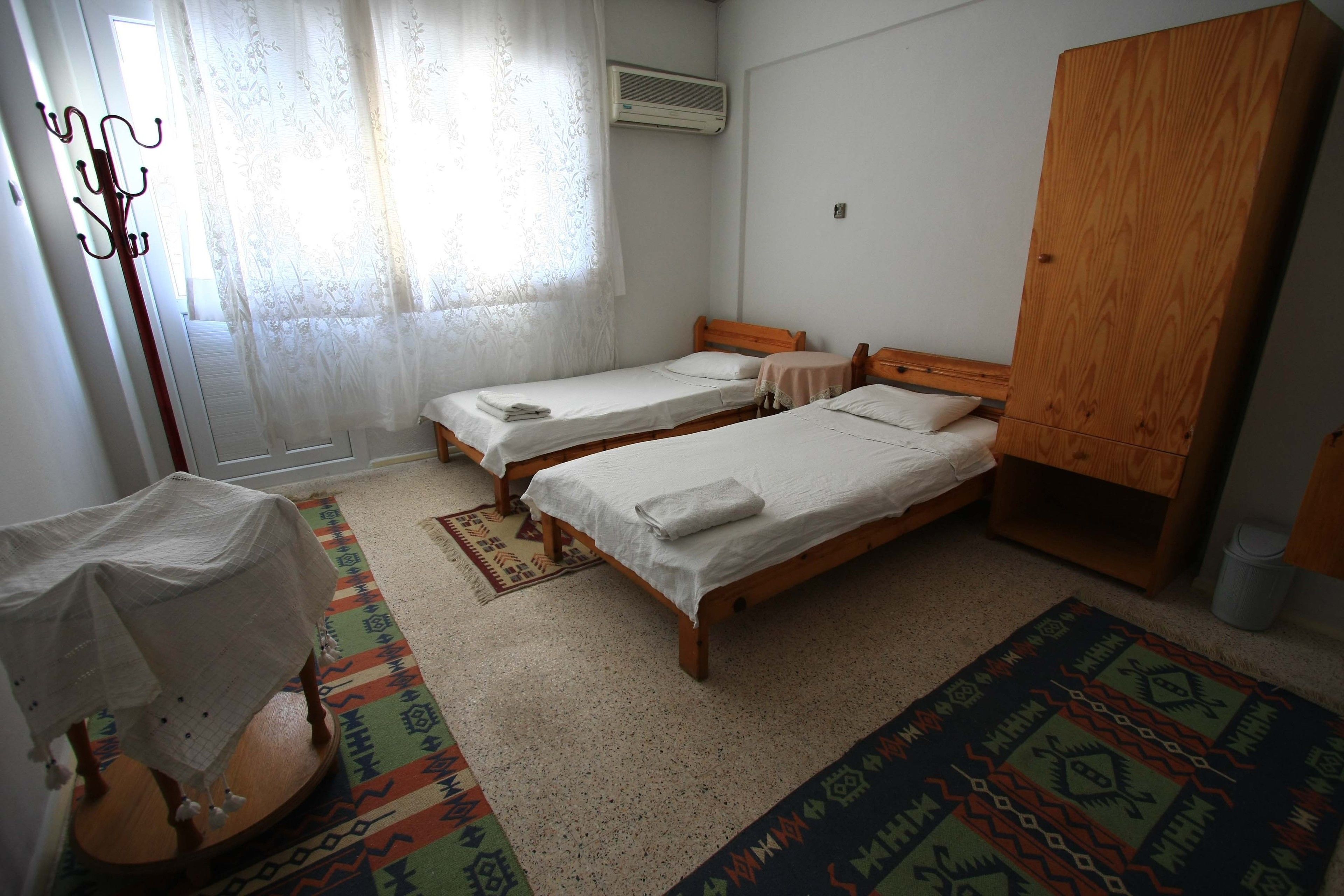 Ein Zimmer mit zwei Holzbetten, einem Kleiderschrank, einem Kleiderständer und einem Fenster mit Vorhängen.