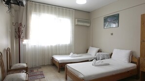 Quarto com duas camas de solteiro, uma cadeira, um cabideiro e uma janela com cortinas finas.