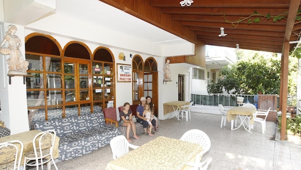Uma área de estar coberta ao ar livre com mesas e cadeiras, teto de madeira e uma placa que indica um ambiente familiar.