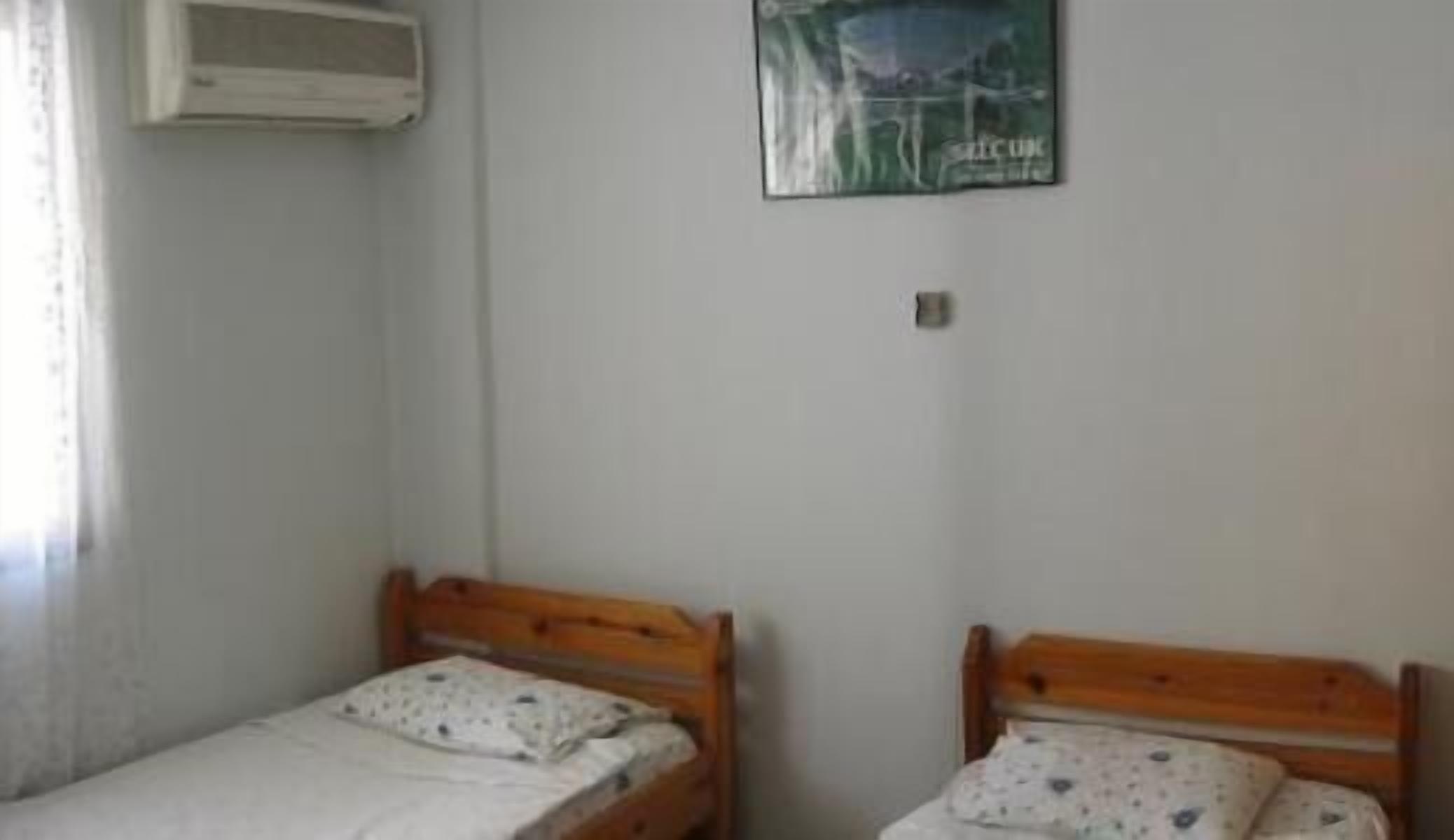 Quarto pequeno com duas camas de madeira, ar condicionado fixado na parede e um quadro emoldurado.