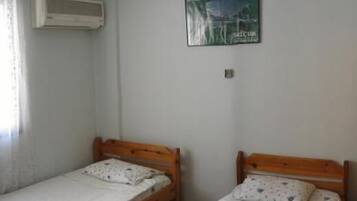 Quarto pequeno com duas camas de madeira, ar condicionado fixado na parede e um quadro emoldurado.