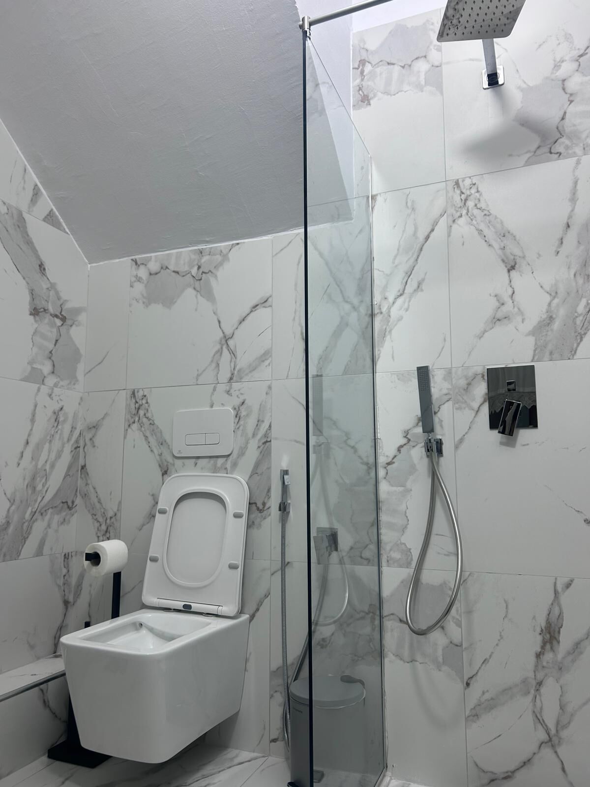 Une salle de bain moderne avec une douche à parois de verre, des toilettes et un mur recouvert de carreaux de marbre.