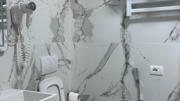 A bathroom with a marble wall, a toilet, a sink, a towel rack, and a shower.