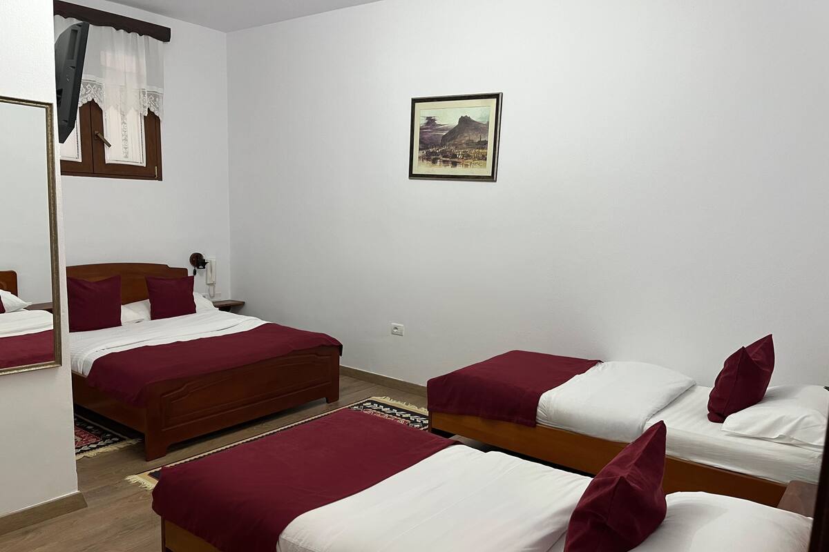 A hotel room with two beds, a wooden headboard, a small bedside table, a telephone, and a framed picture on the wall.
