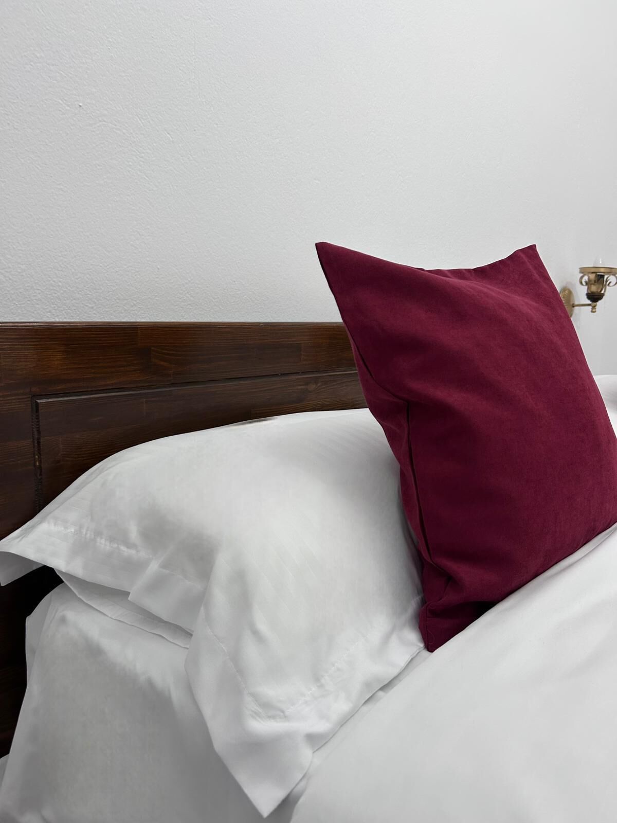 Een bed met witte beddengoed en één marineblauwe kussen.