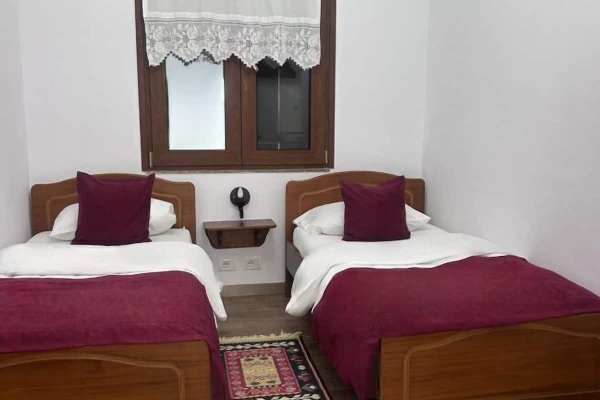 A room with two wooden beds, white bedding, and a window with a lace curtain.