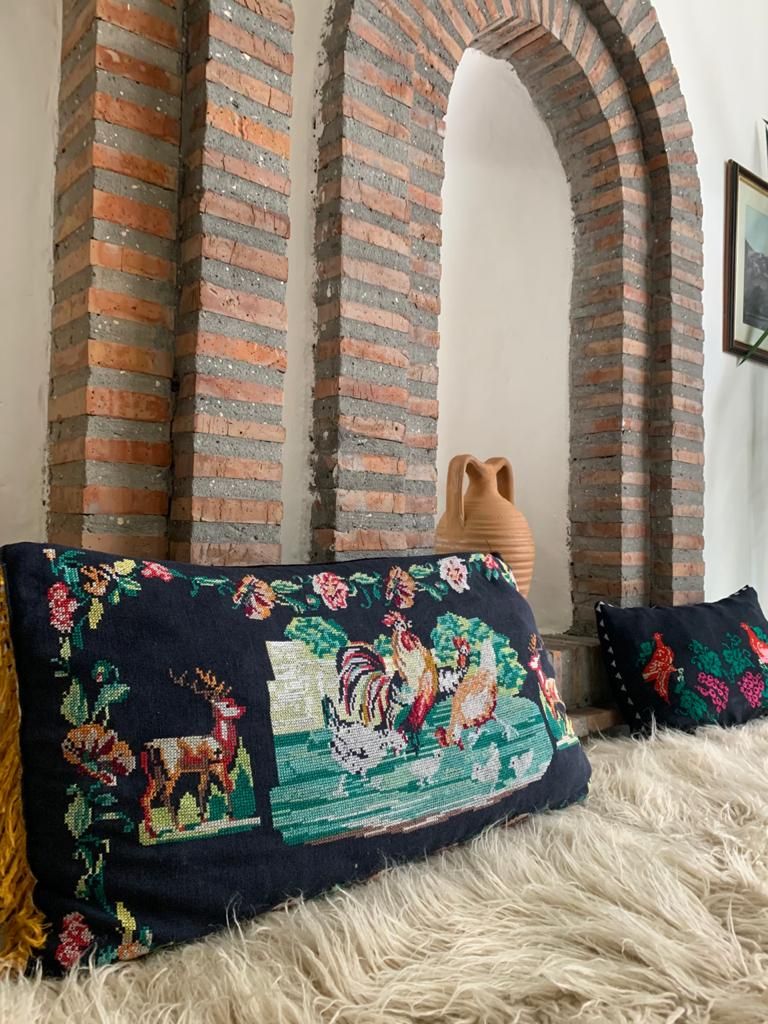 A room with a brick wall, a large vase, and a bed with a fluffy white cover.