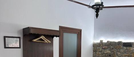 Une chambre à coucher comprenant un lit, une armoire, un portant à vêtements, un ventilateur de plafond, un mur en pierre et un tapis à motifs.