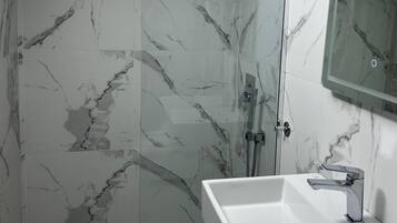 Un bany amb dutxa tancada per vidre, un lavabo blanc i una paret amb un disseny de marbre.