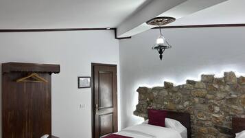 A bedroom with a wooden wardrobe, a stone wall, a bed with white and maroon bedding, and a hanging light fixture.