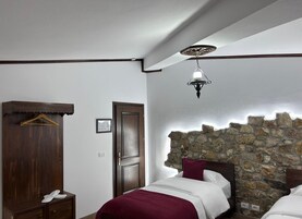 A bedroom with a wooden wardrobe, a stone wall, a bed with white and maroon bedding, and a hanging light fixture.