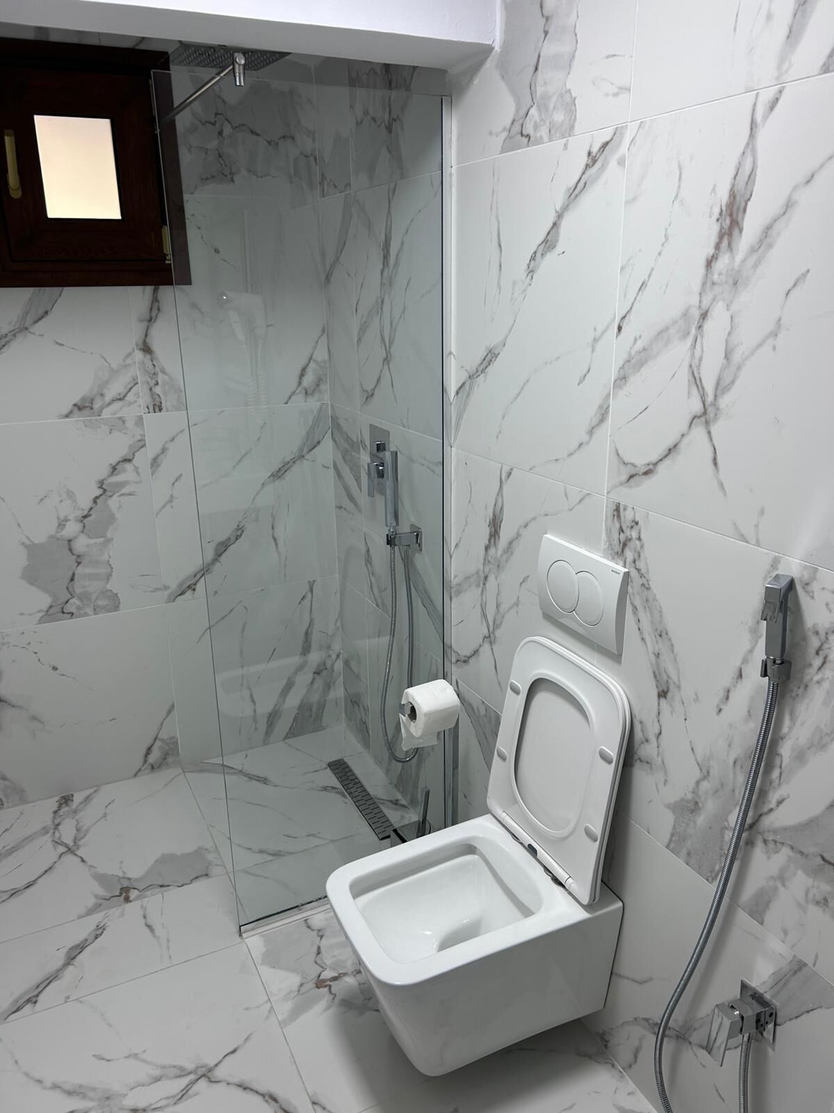 Un baño con ducha acristalada, inodoro con función bidé y paredes con diseño de mármol.