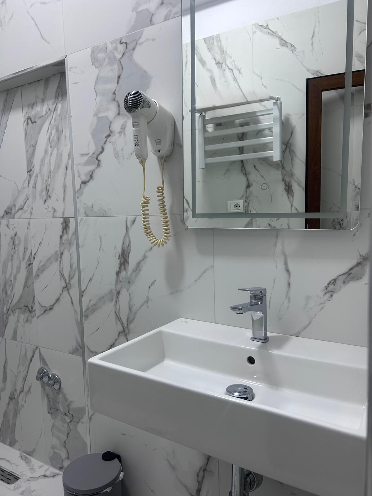 A bathroom with a marble wall, a white sink, a mirror, and a hairdryer.