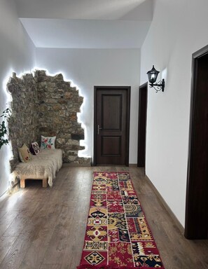 A hallway with a stone wall, a wooden bench, a patterned rug, and a door. - Hotel Berati (Berat)
