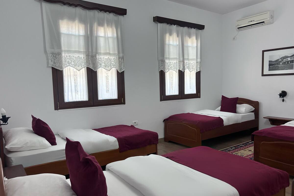 A hotel room with two single beds, a wooden headboard, a nightstand, a lamp, and an air conditioning unit.