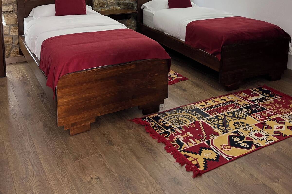 A bedroom with two wooden beds, a stone wall, a ceiling fan, a framed picture, and a patterned rug.