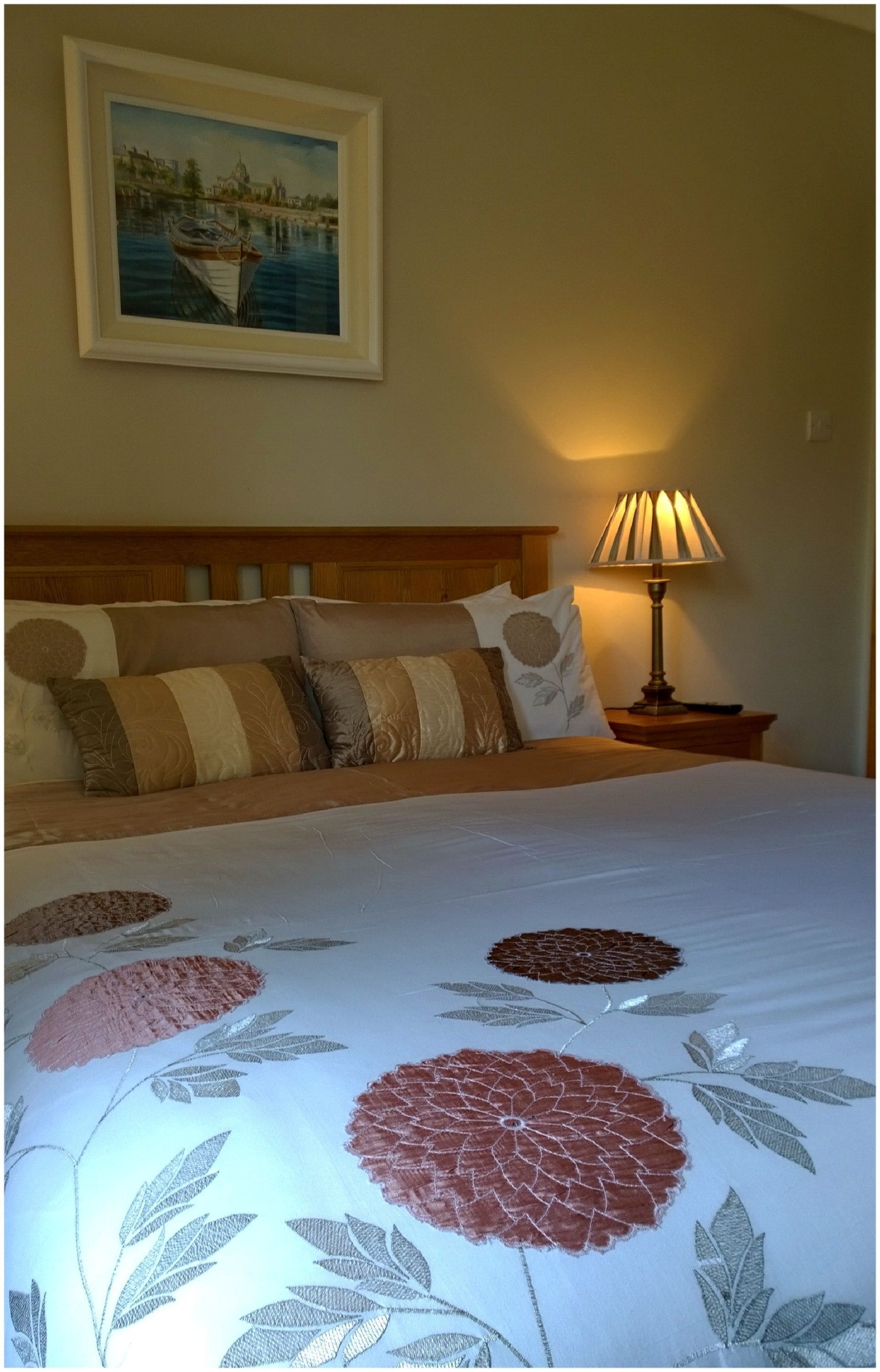 A neatly made bed with a floral bedspread, a painting above the bed, and a bedside lamp.