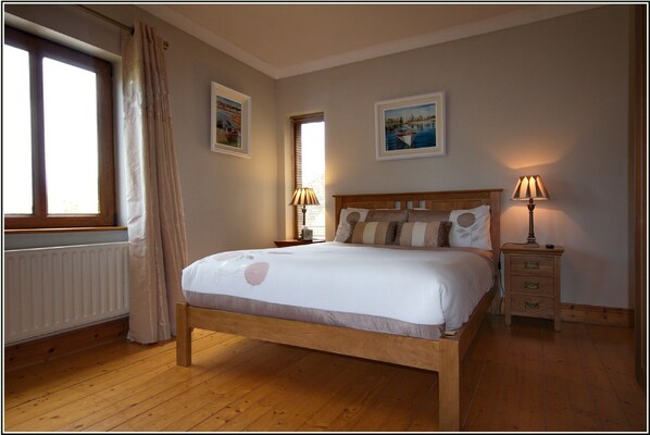 Une chambre à coucher avec un lit en bois, une table de chevet, une lampe et deux fenêtres avec des rideaux.