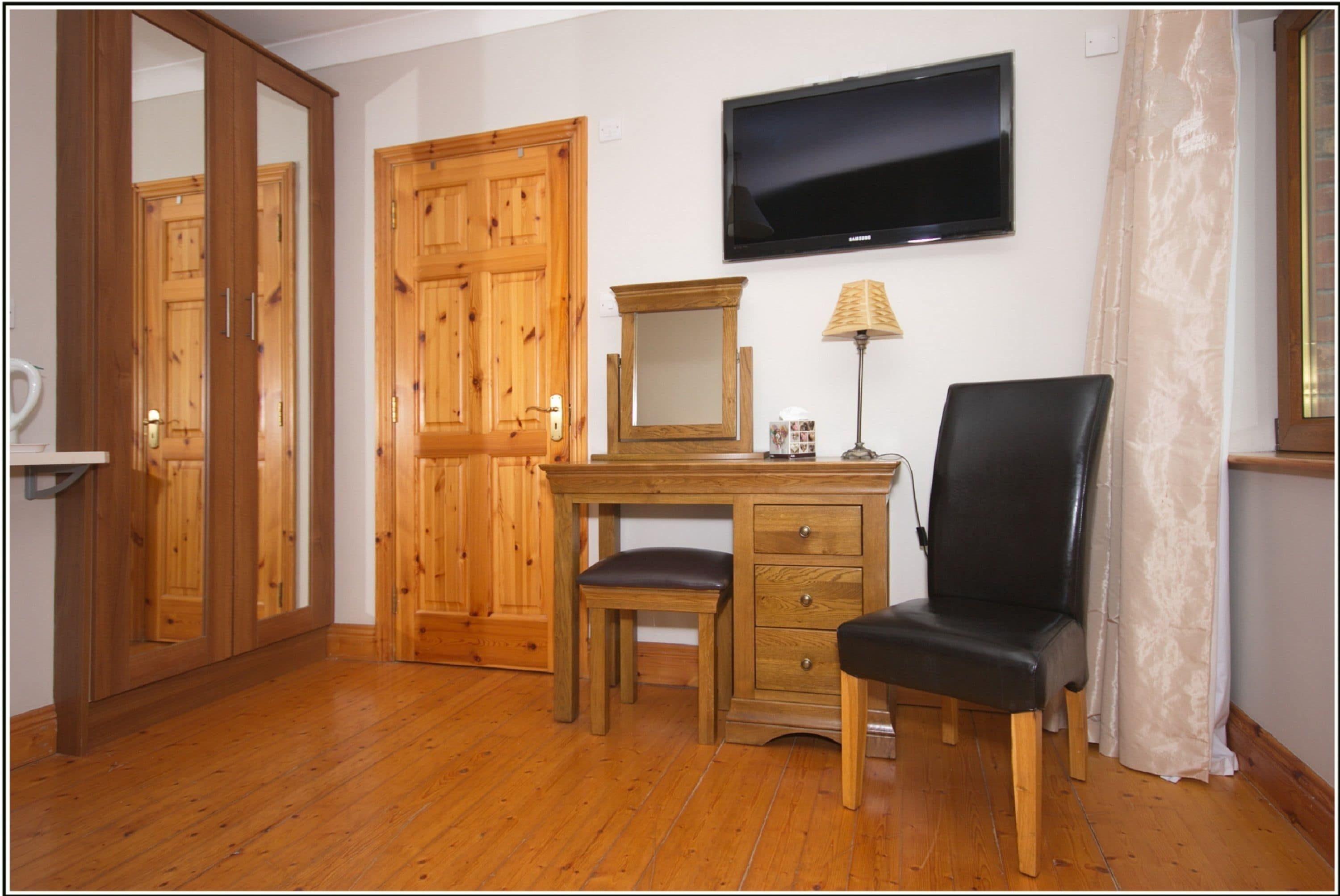 A room with wooden furniture, a desk, a chair, a television, and a mirror.