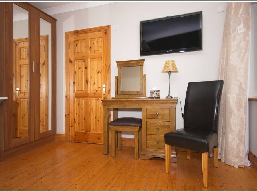 A room with wooden furniture, a desk, a chair, a television, and a mirror.