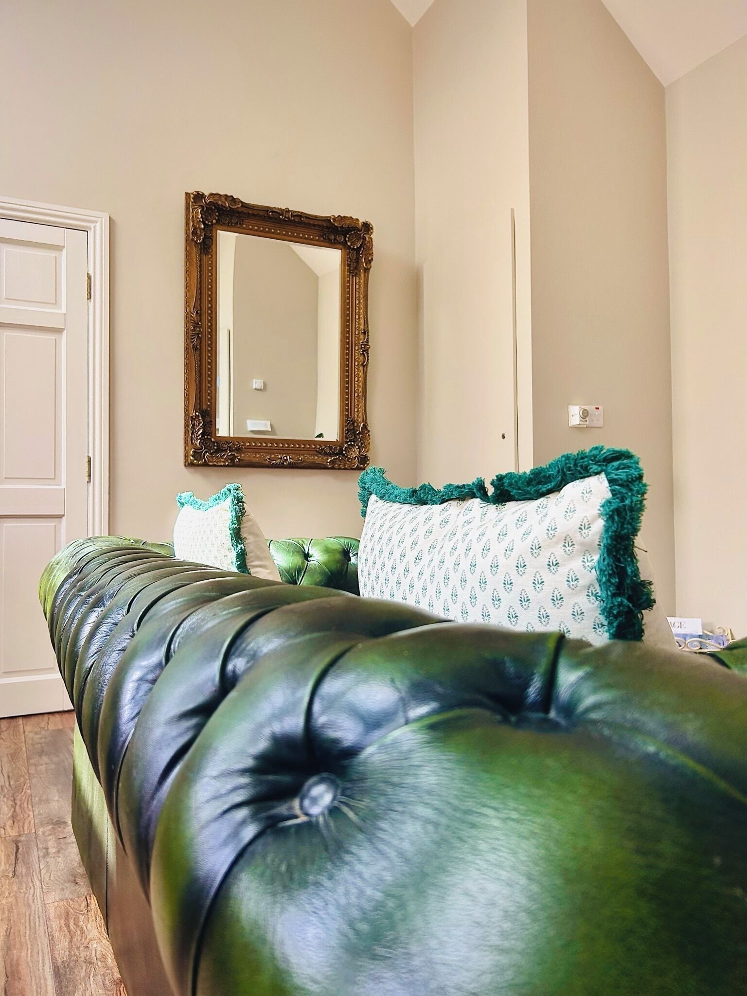 Ein Zimmer mit einem grünen, gepolsterten Sofa, einem großen Spiegel und einer Tür.