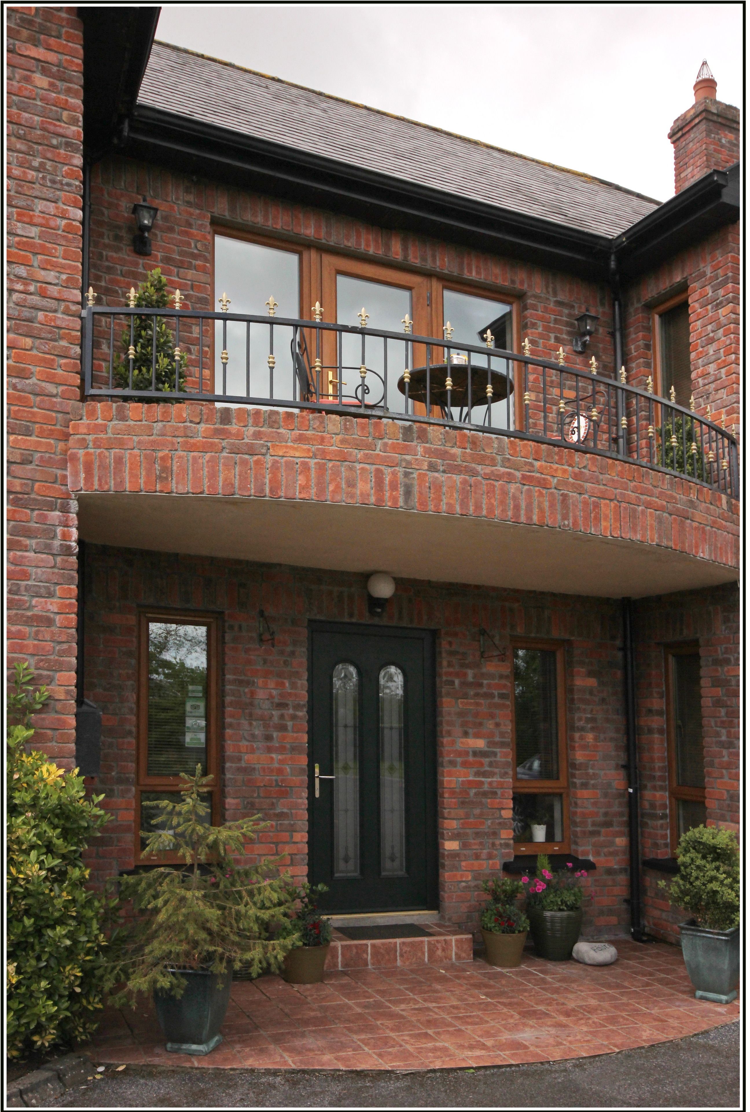 A two-story brick house with a balcony, a front door, and potted plants.