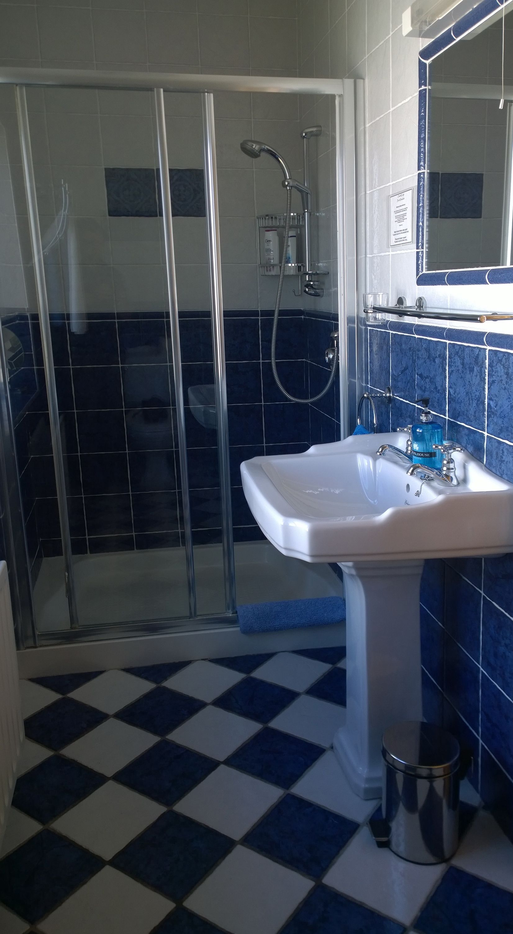 A bathroom with a glass-enclosed shower, a white sink, and blue-tiled walls.